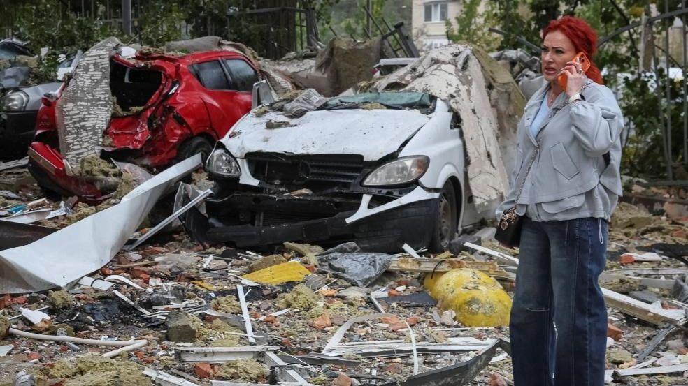 Women in Kyiv hold phones amid damaged neighborhood after a strike
